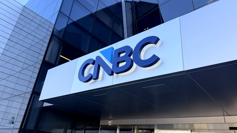 Blauer CNBC-Schriftzug über dem Eingang eines Gebäudes mit Glasfassade.