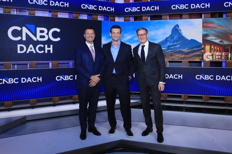 Benjamin Lakatos, Rusmir Nefić und Alexander Schütz stehen in einem Fernsehstudio am Hauptsitz von CNBC vor dem Logo von CNBC DACH.