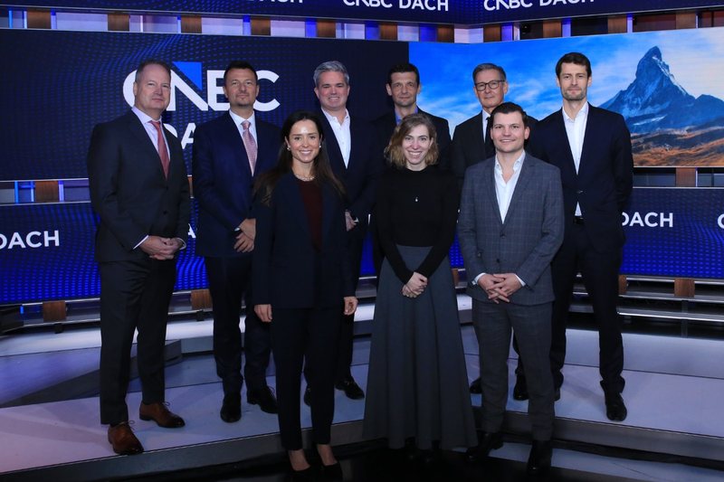 Gruppenfoto in einem Fernsehstudio am Hauptsitz von CNBC, vor Bildschirmen mit dem Logo von CNBC DACH. Hintere Reihe von links: Craig Bengtson, Benjamin Lakatos, KC Sullivan, Rusmir Nefić, Alexander Schütz und Michael Radner. Vordere Reihe von links: Caroline Hadden, Meropi Kylika und Martin Schindler.